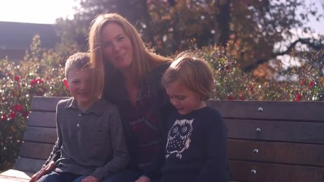 A mother and two kids posing for a picture on a bench at the park, slow motion
