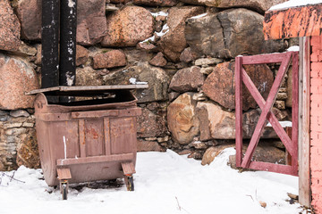 Garbage container and wicket near a stone wall in winter scene.
