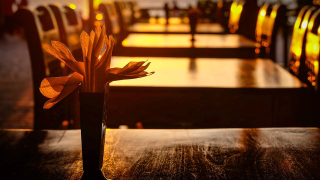Serviettes in a napkin holder standing on a dark wood table in an empty restaurant with emptydark wood chairs