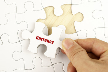 Finance concept. Hand holding piece of jigsaw puzzle showing CURRENCY word.