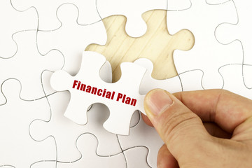 Fototapeta premium Finance concept. Hand holding piece of jigsaw puzzle showing FINANCIAL PLAN word.