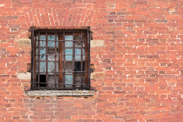 Broken window with lattice on the brick facade of an abandoned building.