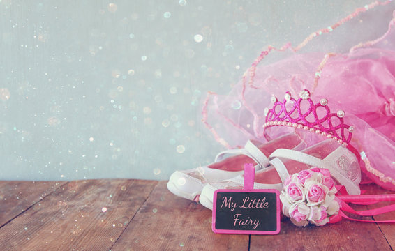 Small girls party outfit: white shoes, crown and wand flowers next to small chalkboards with phrase MY LITTLE FAIRY: on wooden table. bridesmaid or fairy costume. glitter overlay