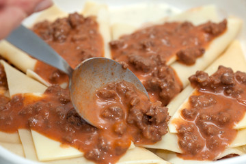 Adicionando salsa bolognesa a los triángulos rellenos para lasagna parmesana