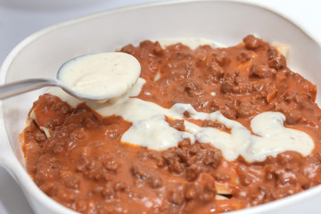 Adicionando salsa blanca a la lasagna parmesana