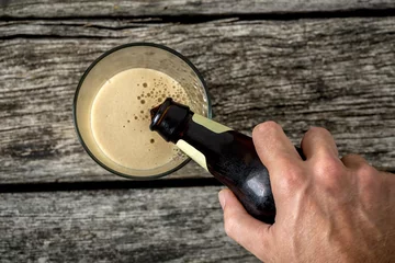 Foto op Plexiglas Top view of male hand pouring dark beer in a glass © Gajus