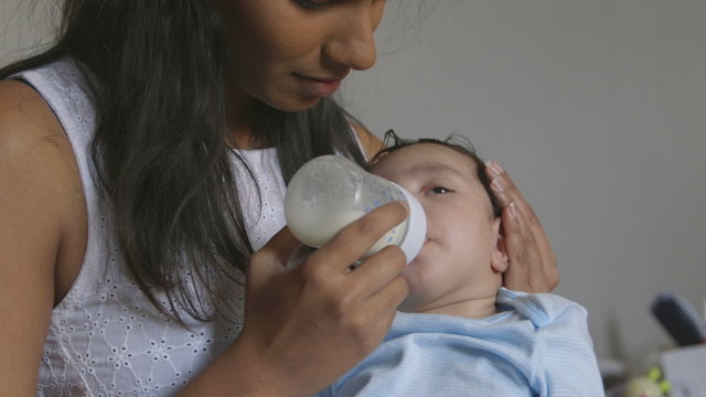 Baby boy fighting off sleep while his mother feeds him a bottle of milk.