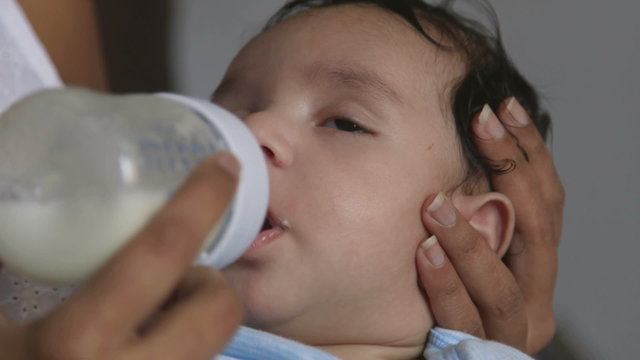 Baby boy fighting off sleep while his mother feeds him a bottle of milk.