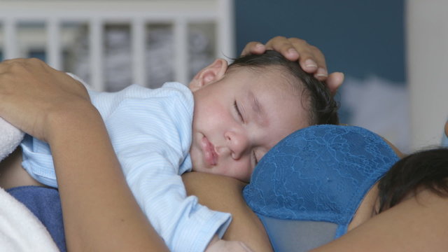 Baby boy having a nap with his mother in her bed. He is sleeping on her chest.