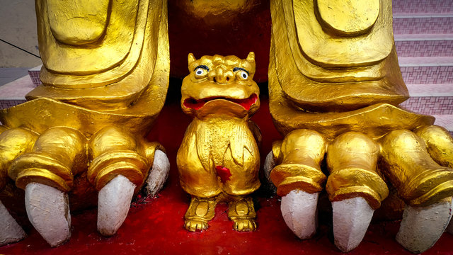 Gold colored small figure between the paw of a bigger statue in a chinese buddhism temple