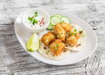 Crispy fried fish on a homemade tortilla on a light  rustic wooden background
