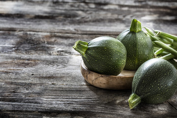 vegetable still life - round zucchinis and green beans set on genuine old wood background for vegetarian home-made cuisine, studio shot.