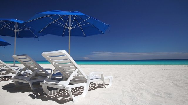 Caribbean beach with blue sun umbrellas and white plastic beds