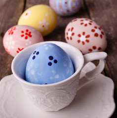 Easter painted blue egg in white cup on wooden rustic background. Some eggs near.