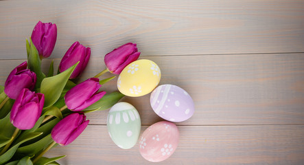 Easter painted eggs on wooden light background with spring pink bouquet tulips. Empty space for text. Top view.