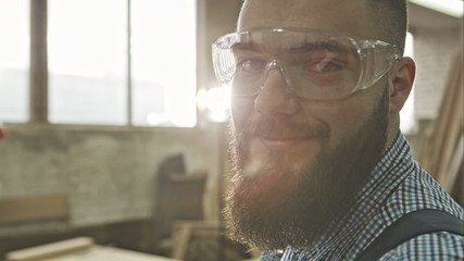 Closeup view of one handsome young adult man worker with a beard and goggles. RAW video record.