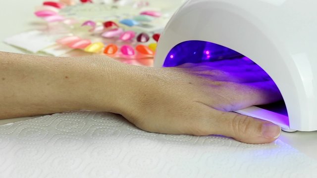 Manicure in process - putting hand and curing gel varnish in nail LED lamp, procedure of polymerization 
