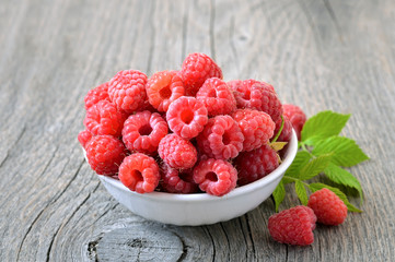 Raspberries in white bowl on wooden table