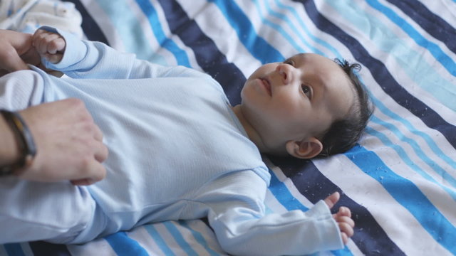 Baby boy is lying on his daddy's bed, who has just finished getting him dressed.