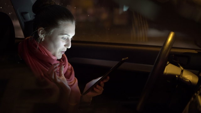 Profile of emotional girl sitting in the car and using tablet. 4K