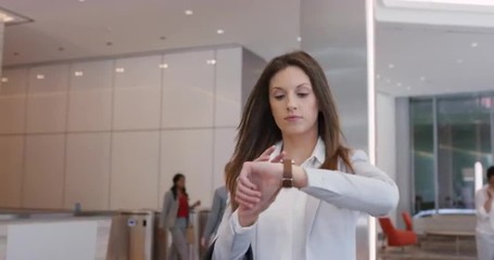 Attractive successful businesswoman leaving corporate office lobby checking smartwatch