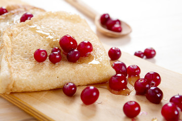 Pancakes with honey and cranberries on a wooden board