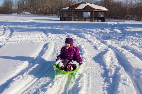 A little girl sitting on a sleigh being pulled along a snowmobile trail