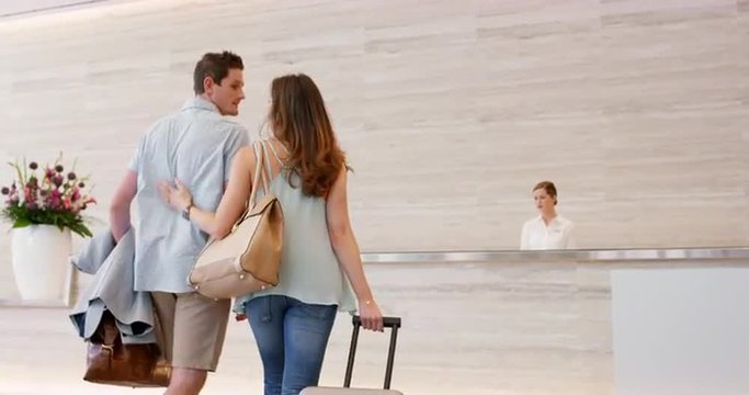 Attractive happy couple arriving at hotel reception travelling on vacation
