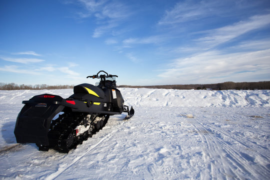 A snowmobile sitting on a snow hill with a wispy blue sky above