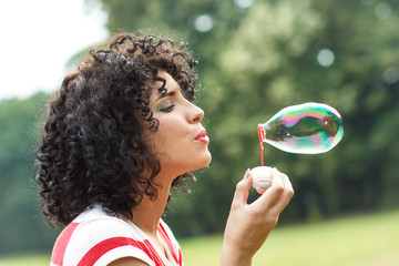 Portrait of beautiful woman blowing bubbles in park. - Powered by Adobe