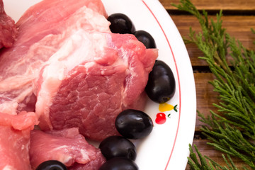 Dish of pork meat, olives  and green branch on wooden background
