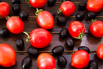 Black olives, cherry tomatoes and green branch on wooden background 