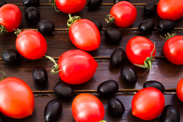 Black olives, cherry tomatoes and green branch on wooden background 