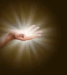 Connecting to the Divine Source - a male hand with palm open  glowing with light energy on a dark...