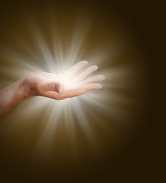 Connecting to the Divine Source - a male hand with palm open  glowing with light energy on a dark warm brown background with plenty of copy space