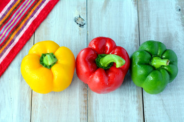 Flat lay of a yellow, red and green capsicum on a wooden table