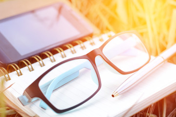 Notebook glasses pen and smart phone on the grass.