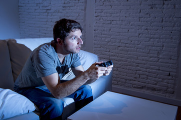 young excited man at home sitting on living room sofa playing video games using remote control...