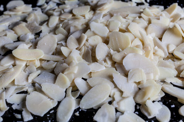 Flaked almonds heap on black surface from side closeup