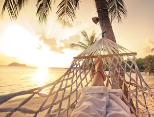 Female legs in a hammock on a background of the sea, palm trees and sunset. Vacation concept - Powered by Adobe