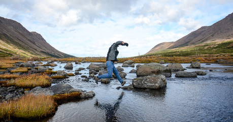 Man crosses a stream jumping rock to rock