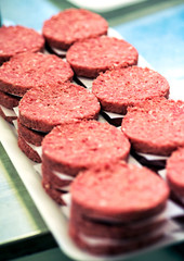 Two rows of stacked red beef patties on a tray