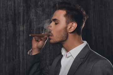 Side view of a cheeky man in suit on the grey background smoking