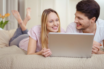 Fototapeta premium paar liegt auf dem bett und schaut ein lustiges video am notebook an