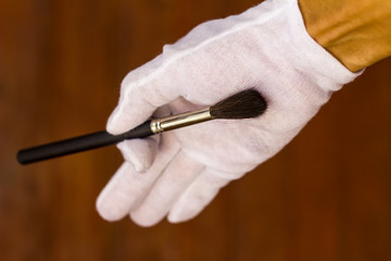 White gloved hand holding a paintbrush.