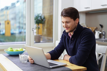 mann sitzt zuhause am tisch und liest eine nachricht am laptop