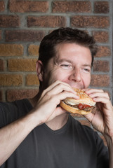 White middle aged man bites into hamburger with ketchup on a sesame bun