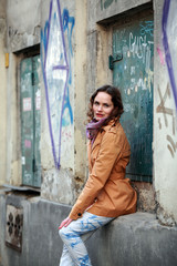 Beautiful brunette woman with beige coat sitting at a house with graffiti