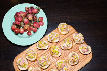 Fototapeta na wymiar Wooden tray of appetizers on pallet coffee table at banquet with bacon, green herbs and turquoise ceramic plate with grapes.