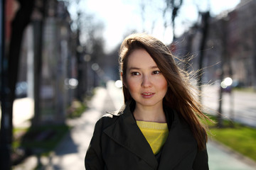 Beautiful Asian woman with yellow sweater and olive coat walking on the street